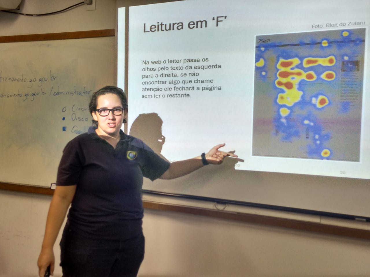 Instrutora Camila Freitas apontando para uma projeção feita pelo datashow no quadro branco. A projeção refere-se à leitura em F.