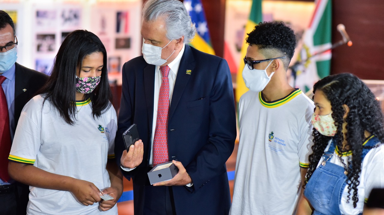 O governador Ronaldo Caiado entrega smartphone a Thauana Guadalupe Lima Barbosa, de 16 anos, em meio a outros estudantes que também serão beneficiados