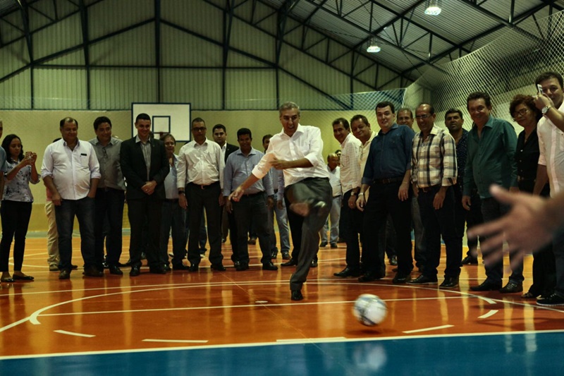 José Eliton chuta bola de futebol para o gol em ginásio de esporte acompanhando por auxiliares e autoridades municipais