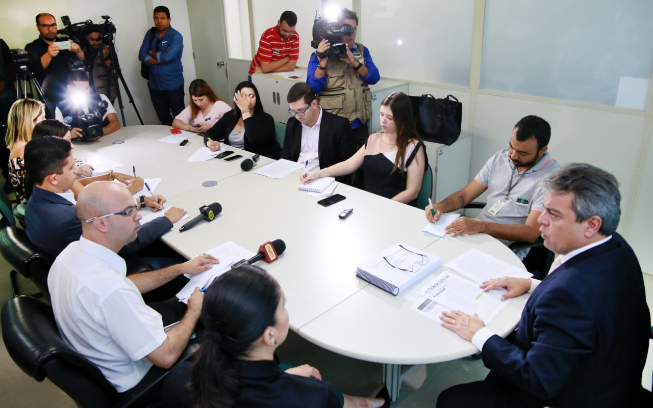 Secretário, sentado à mesa, conversa com jornalistas