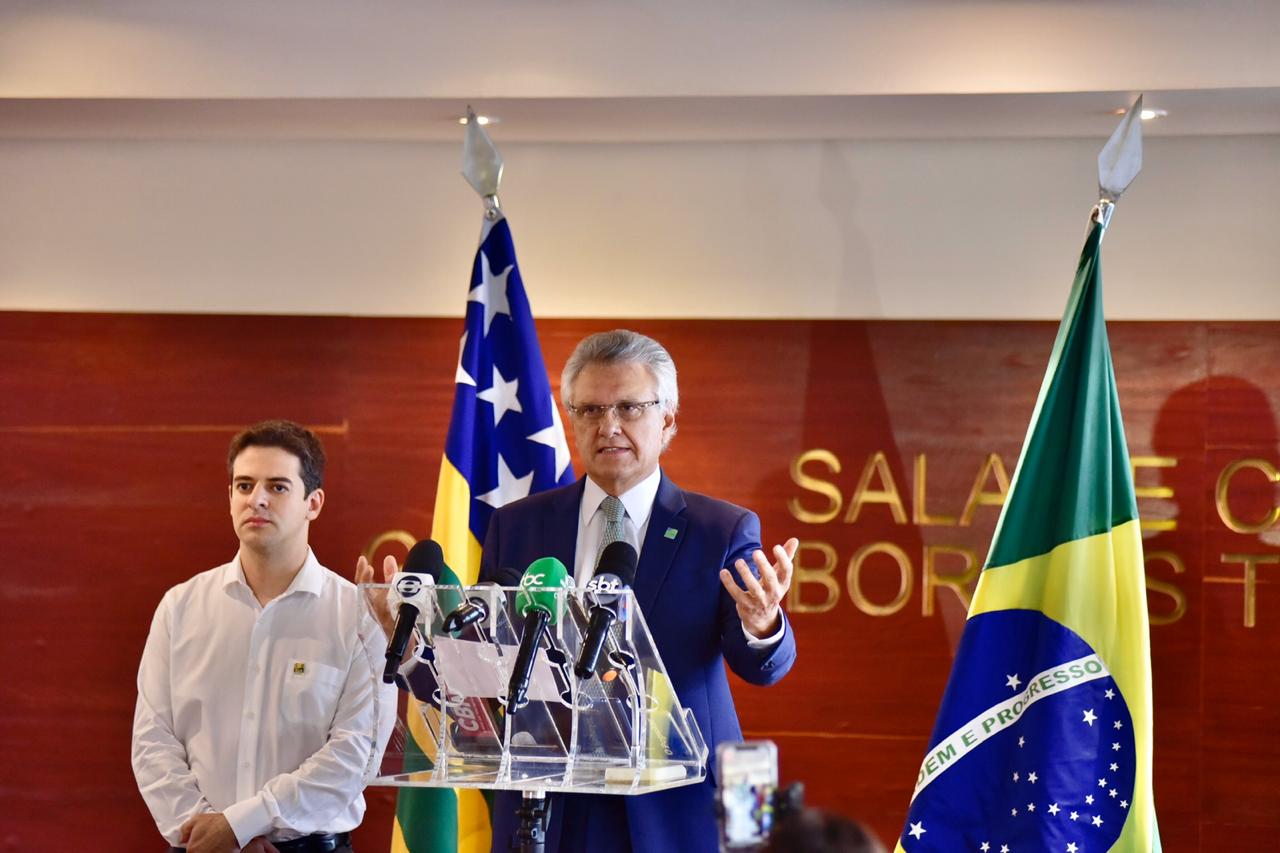Governador Ronaldo Caiado utiliza púlpito para falar à imprensa em entrevista coletiva. Ao lado dele, está posicionado o secretário de saúde, Ismael Xavier.