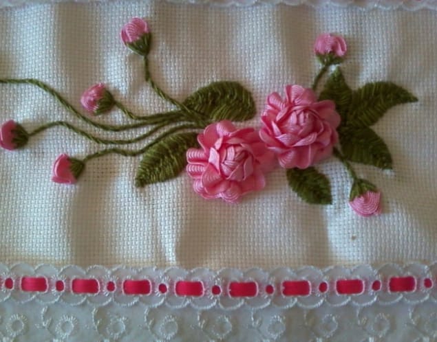Flores rosa e folhas verdes bordadas em tecido de fundo branco.