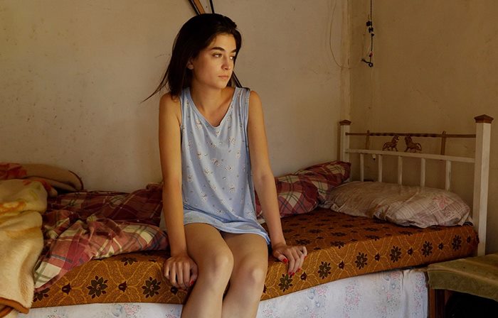 Cena do filme Yara, a protagonista de mesmo nome aparece sentada em uma cama.