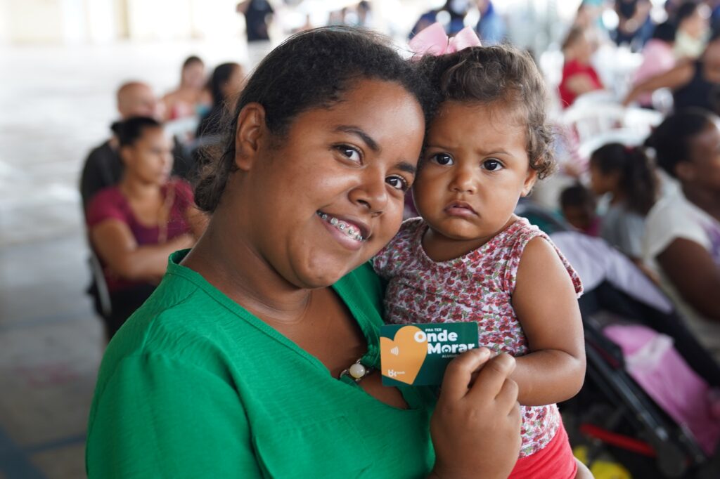 Beneficiária com bebê no colo segurando cartão do Aluguel Social